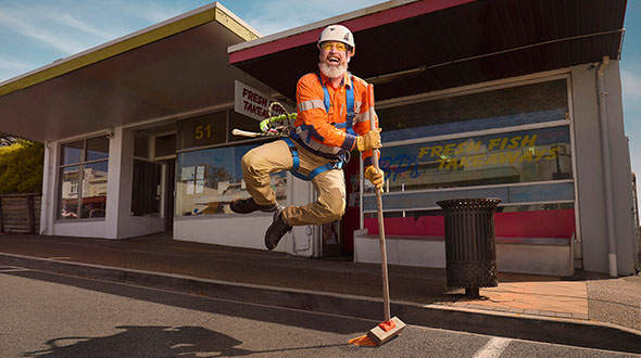 Leif is leaping into the air with broom in hand in front of a shop front