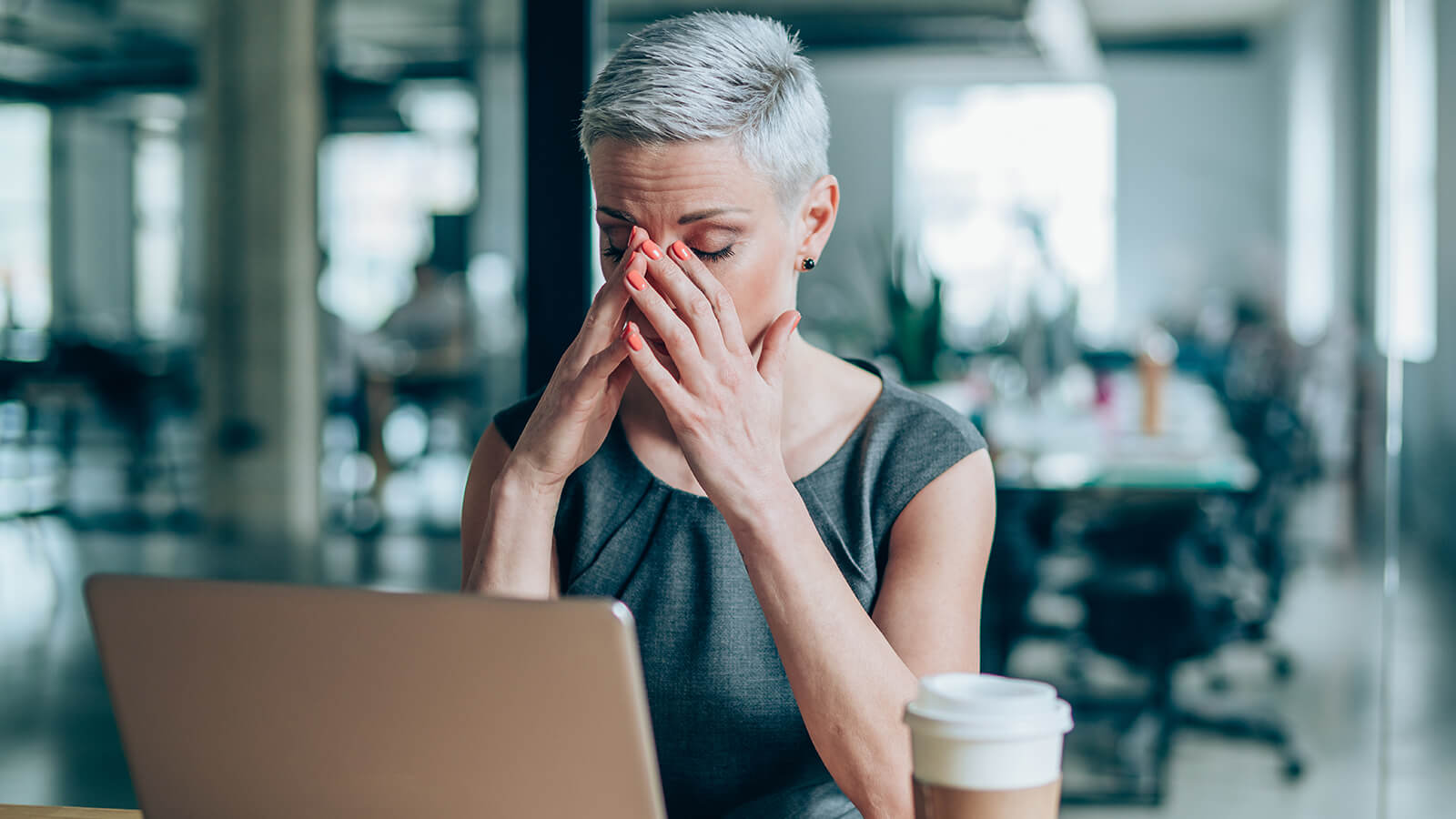 A woman rubs her eyes while working at her laptop
