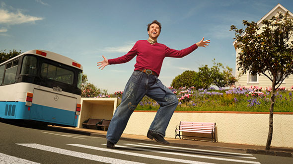 Alex is dancing with arms outstretched on a pedestrian crossing. A bus in the background at a bus stop.